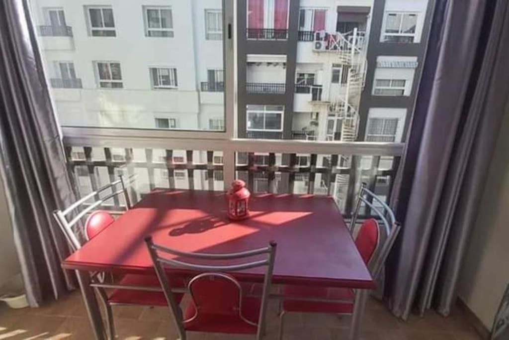 d'une table et de chaises rouges sur un balcon avec fenêtre. dans l'établissement Holikeys - Agadir - 2 Ch - El Houda 001, à Agadir