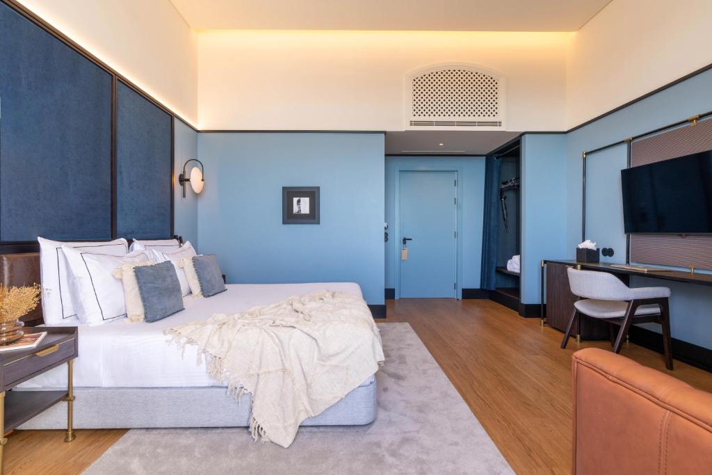 A blue-toned bedroom with a large bed, wall-mounted television and dedicated desk.