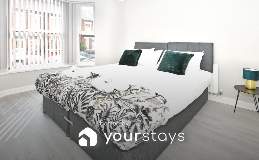 um quarto com uma cama grande com lençóis brancos e almofadas verdes em Heathfield House by YourStays em Crewe