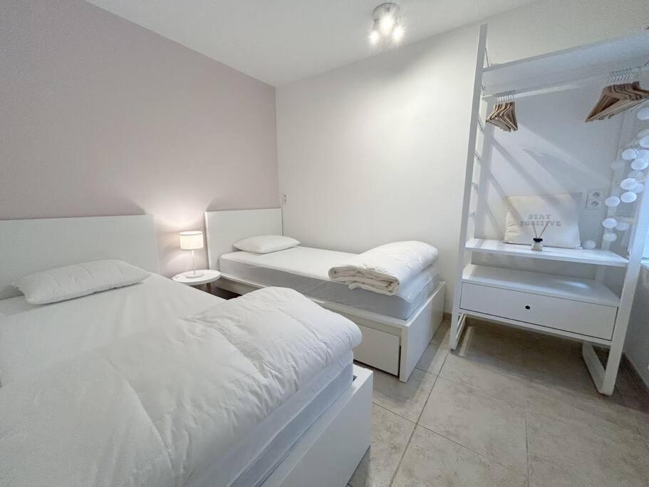 a white bedroom with two beds and a window at Appartement met 2 slaapkamers-VAYA G002 in De Panne