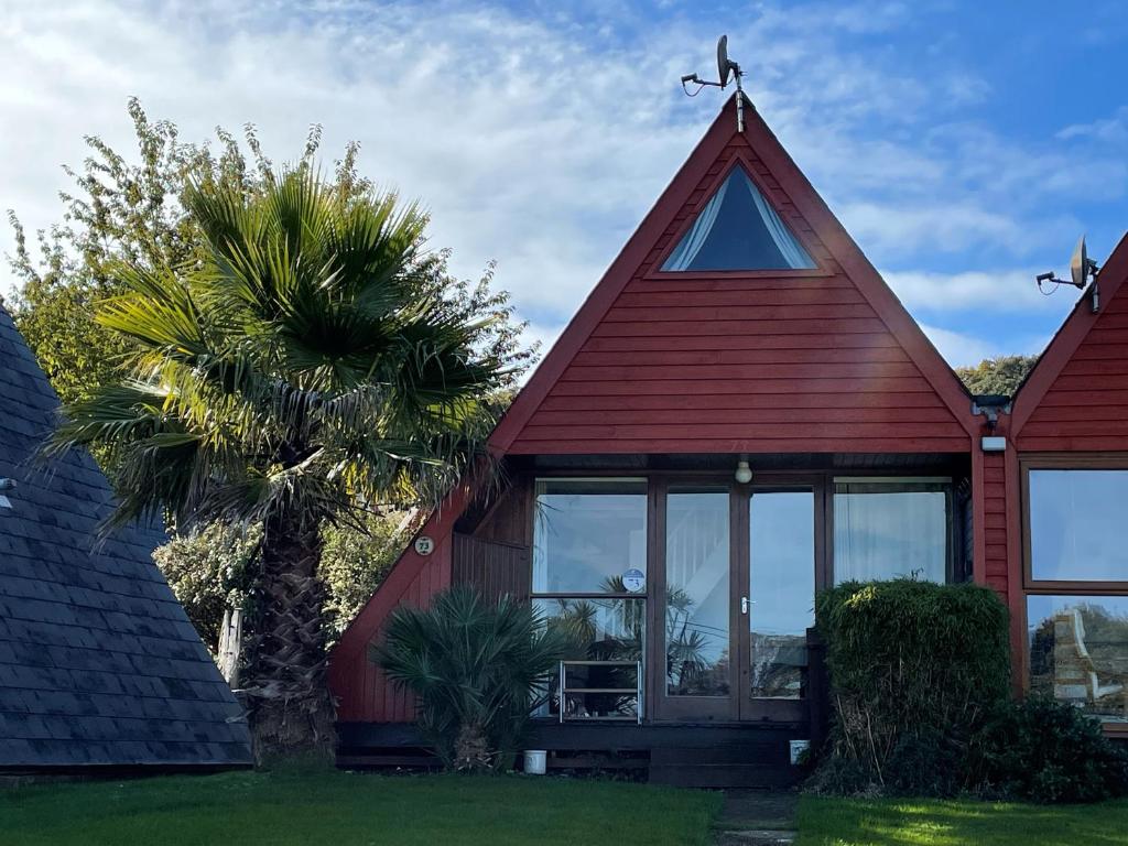 a red house with a triangular roof and a palm tree at 73 Palm Lodge in Kingsdown