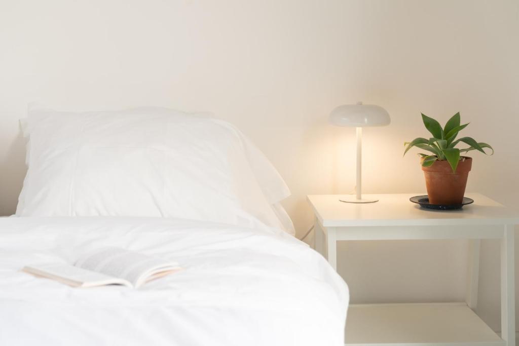 a white bed with a book and a lamp on a table at Vitaminas - Casa de Playa y Café in Punta del Este