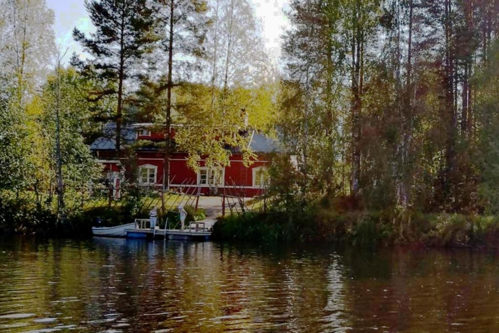 uma casa vermelha com um barco na água em Paritalokolmio joen rannalla em Haapavesi