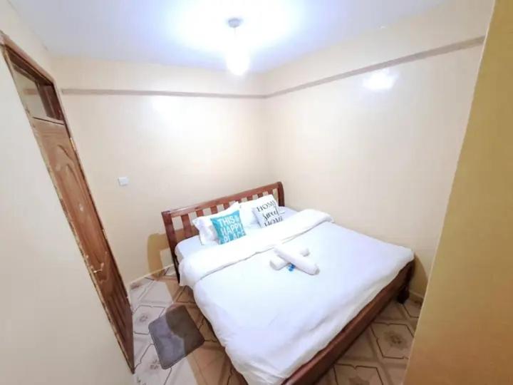 Schlafzimmer mit einem Bett mit weißer Bettwäsche und blauen Kissen in der Unterkunft IMMARA BNB in Nakuru