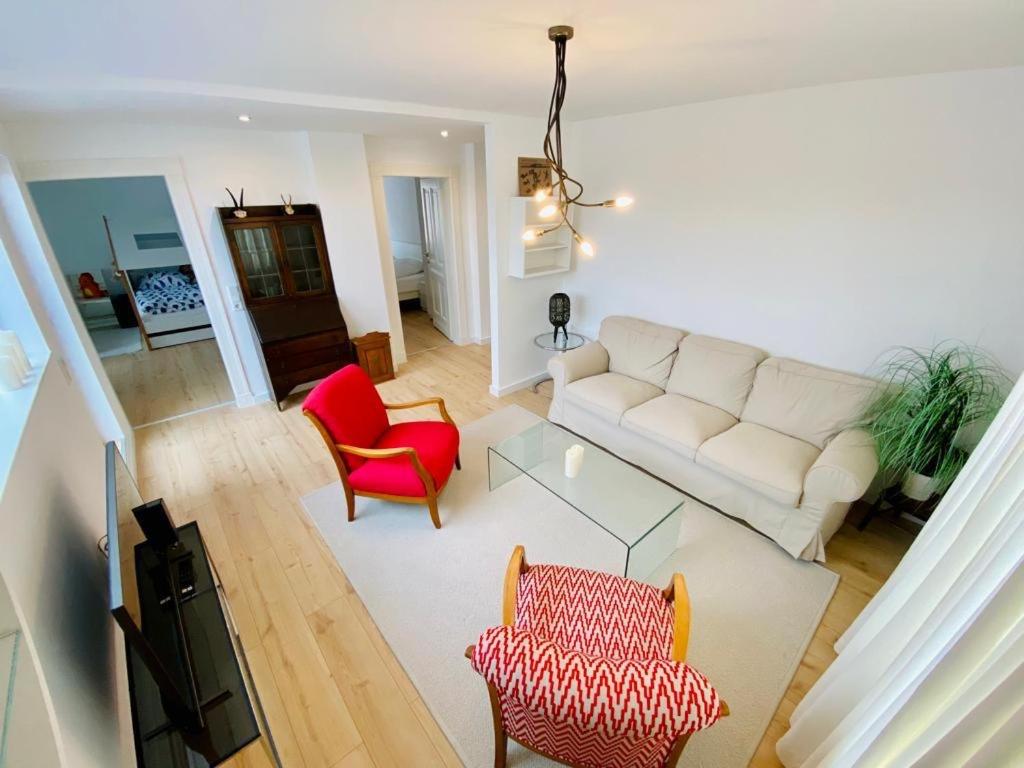 uma sala de estar com um sofá branco e cadeiras vermelhas em Cute Apartment - Detmold city center - large kitchen, bath, south facing balcony - free parking and wifi em Detmold