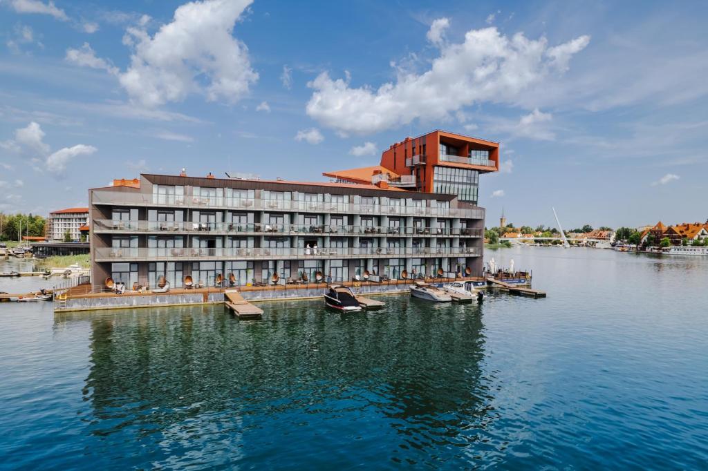a hotel on a lake with boats in the water at Hotel Mikołajki Leisure &amp; SPA in Mikołajki