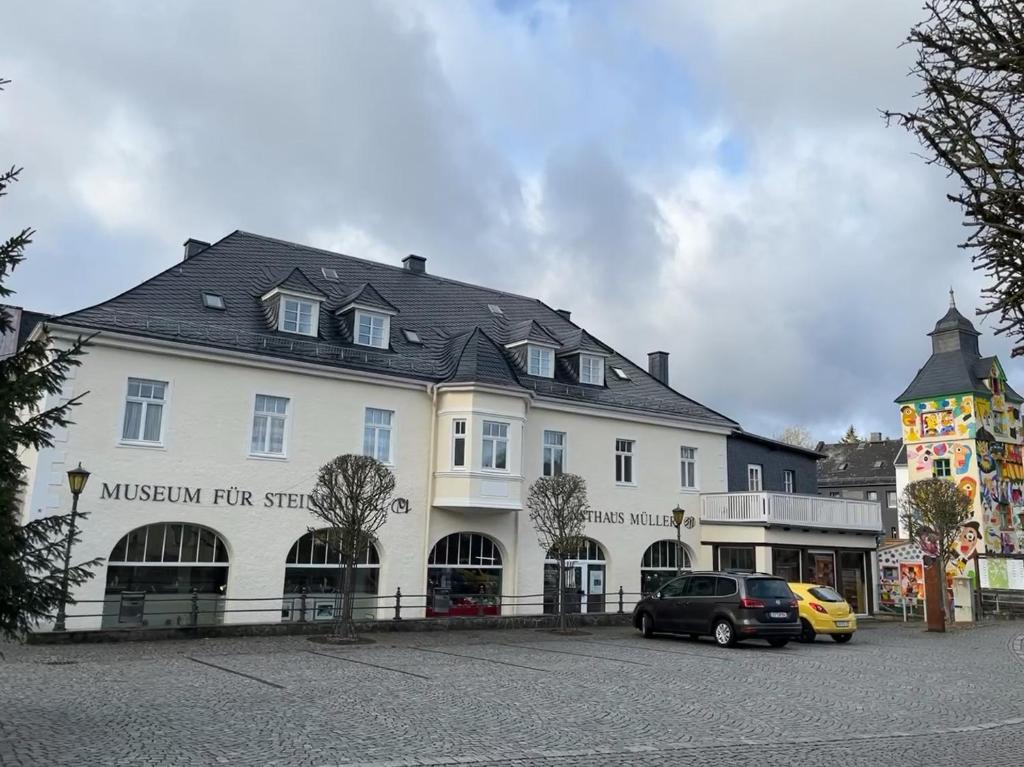 un grand bâtiment blanc avec des voitures garées devant lui dans l'établissement Ferienwohnung im ehemaligen Rittergut, à Wurzbach