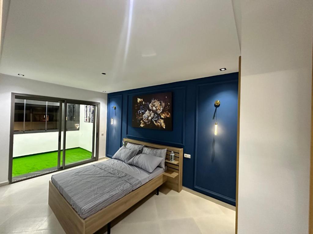 een slaapkamer met blauwe muren en een bed met een raam bij Appartement Bouznika Plage in Bouznika