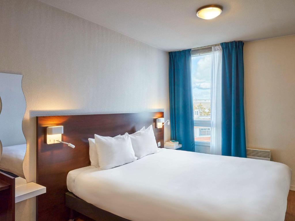 - une chambre avec un grand lit blanc et une fenêtre dans l'établissement Aparthotel Adagio Access Paris Saint-Denis Pleyel, à Saint-Denis