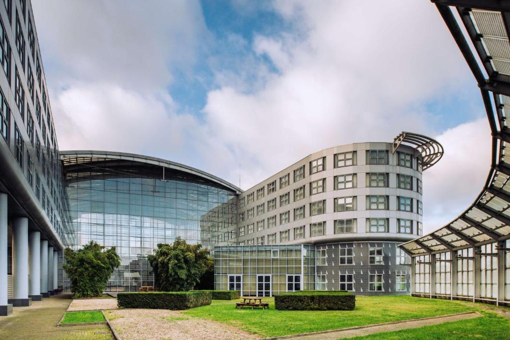 un gran edificio de cristal con un parque delante de él en The Atrium Hotel & Conference Centre Paris CDG Airport, by Penta en Roissy-en-France