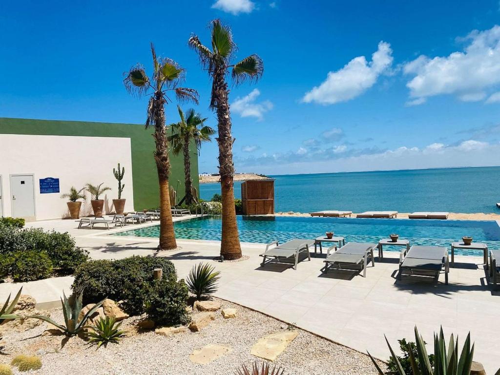 a pool with palm trees and chairs and the ocean at Dakhla South Bay in Dakhla