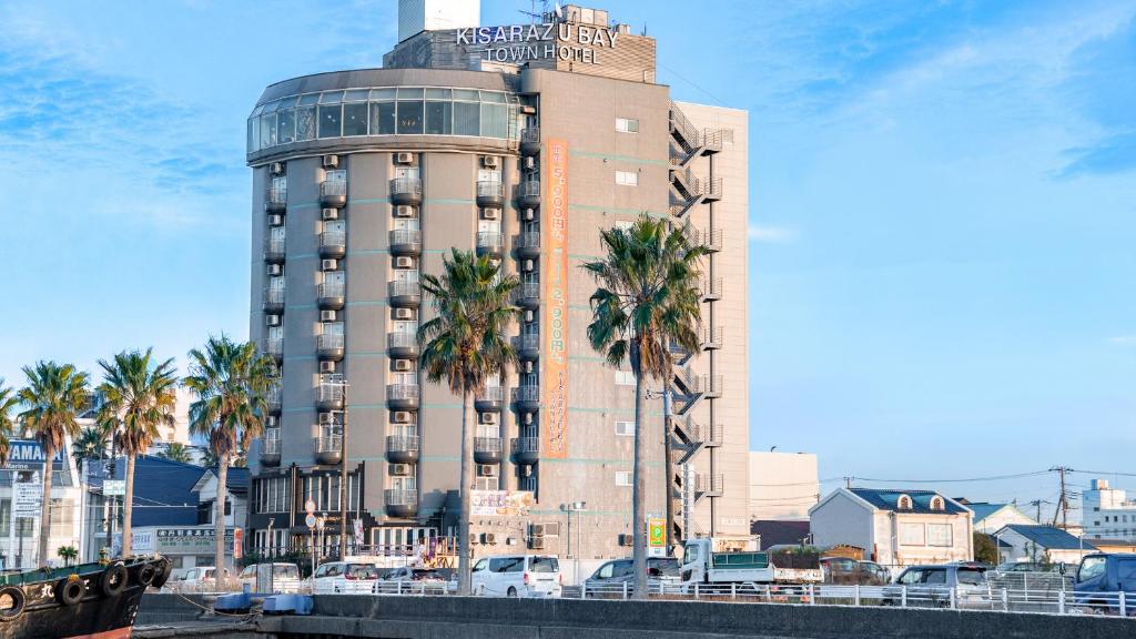 a tall building with palm trees in front of a river at kisarazu bay Town Hotel in Kisarazu