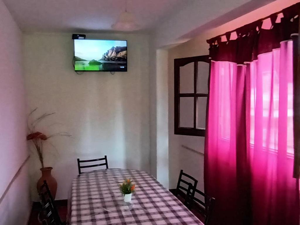 Habitación con una mesa con cortinas rosas y TV. en ARROYO SERRANO-MINA CLAVERO en Mina Clavero