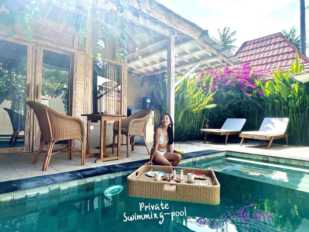 a woman is sitting next to a swimming pool at GiliZen Resort - Private Pool Villas in Gili Islands