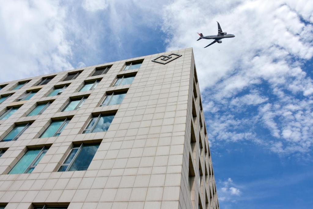 Um avião sobrevoa um edifício alto. em Cordis, Beijing Capital Airport By Langham Hospitality Group em Shunyi