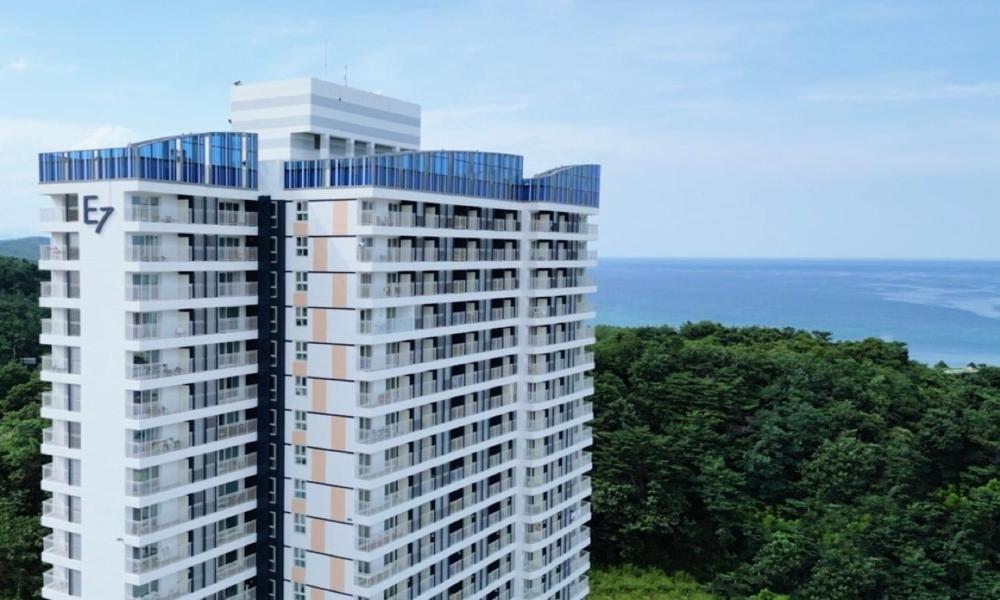 a tall white building with blue windows next to the ocean at E7 YANGYANG JUKDO in Yangyang