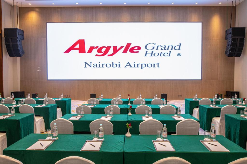 a conference room with green tables and chairs and a large screen at Argyle Grand Hotel Nairobi Airport in Nairobi