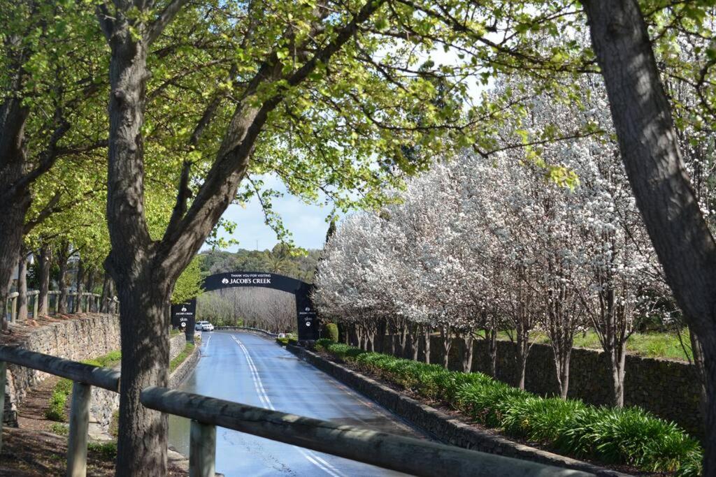 a tree lined road with a bridge and flowering trees at Blackbird Cottage - Stunning views & farm animals in Tanunda