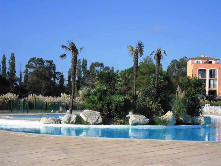 a swimming pool with palm trees and a building at GASDON - Golfe de St-Tropez - Gassin - Studio cabine dans résidence avec piscine bord de mer in Gassin