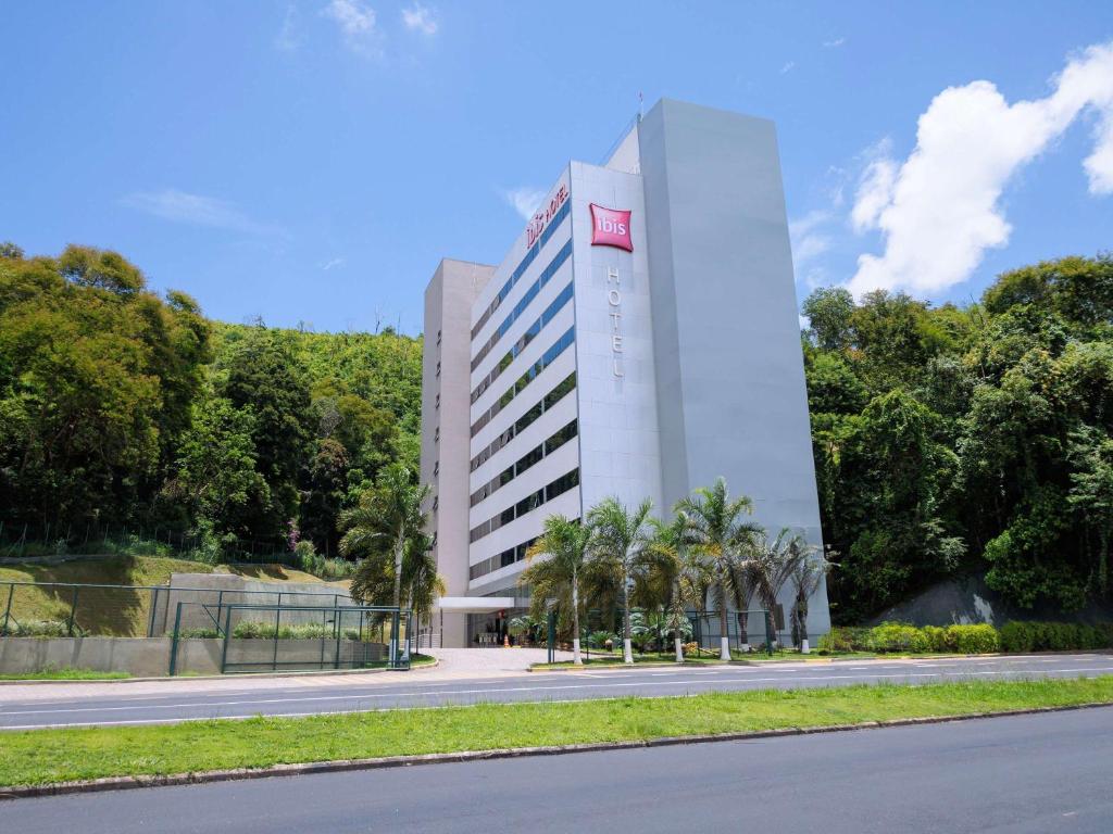 a tall white building with palm trees in front of a road at ibis Juiz de Fora in Juiz de Fora