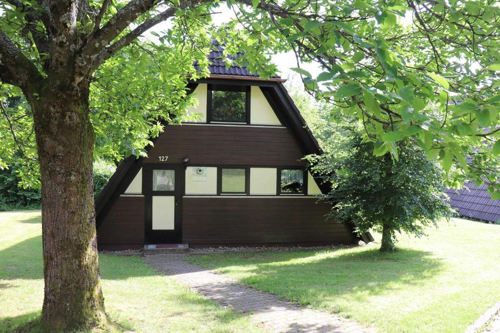 een bruin huis met een witte deur en een boom bij Ferienhaus Winnetou Im Abendrot 127 in Waldbrunn