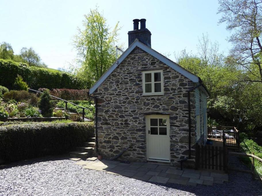 um pequeno edifício de pedra com uma porta branca em Hafannedd Cottage - riverside views em Corwen