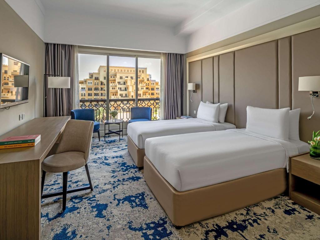 a hotel room with two beds and a desk at Rixos Bab Al Bahr - Ultra All Inclusive in Ras al Khaimah