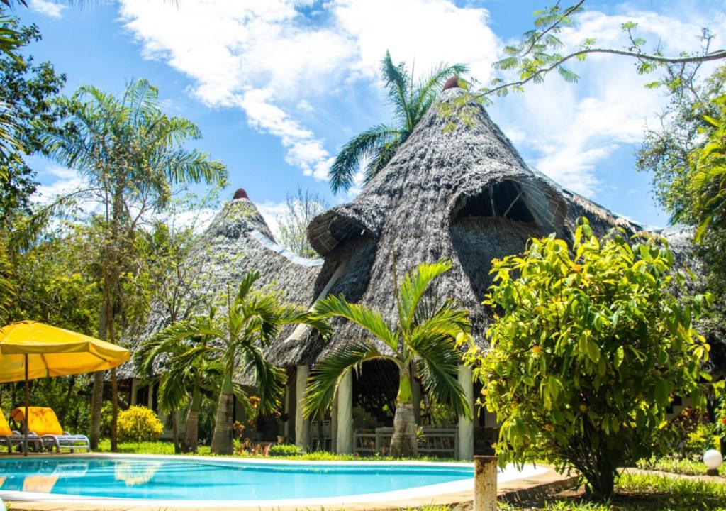 een resort met een zwembad en een rieten gebouw bij Le Grand Forest dreams Resort in Ukunda