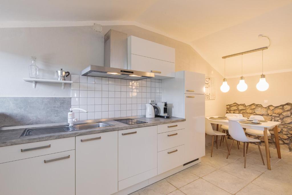 a kitchen with white cabinets and a table and a dining room at Apartments Lina in Vrh