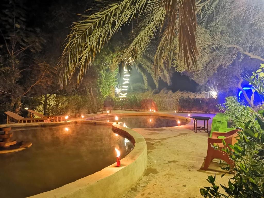 einen Pool in der Nacht mit einem Tisch und Lampen in der Unterkunft Desert Escape siwa -with palm & olive Garden - Hot Spring in Siwa