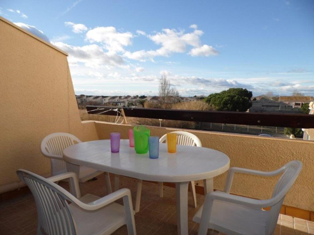 une table blanche et des chaises sur un balcon avec vue dans l'établissement Charmant Studio Cabine Mezzanine avec Terrasse et Piscine à Marseillan - 6 Couchages - FR-1-326-437, à Le Castellas