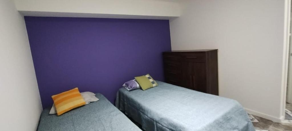 two beds in a room with a purple wall at Departamento Nuevo in Punta Arenas