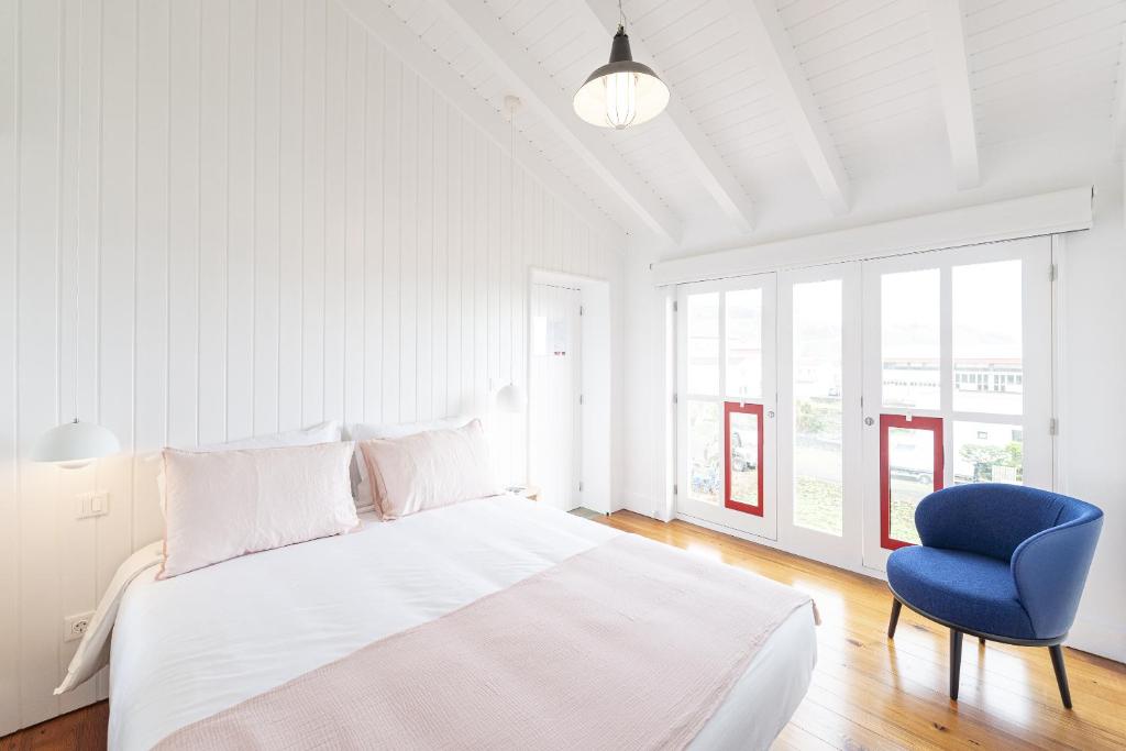 1 dormitorio blanco con 1 cama y 1 silla azul en Engenho Hostel en Lajes do Pico