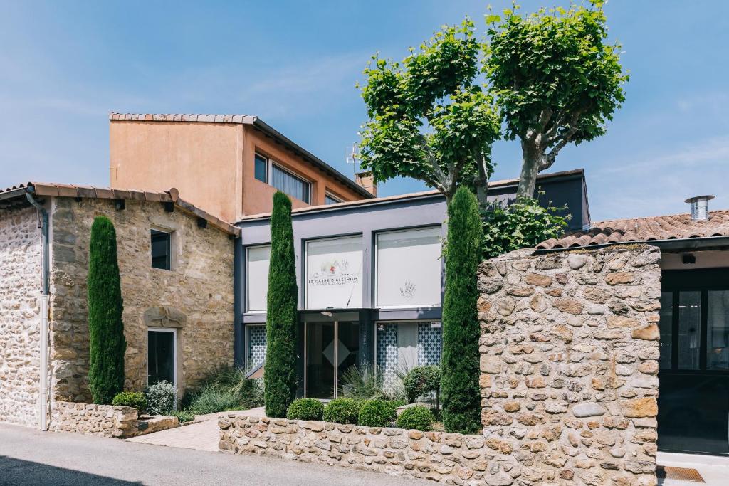 un edificio con una pared de piedra y árboles en Le Carré d'Alethius Logis Hôtel Restaurant, en Charmes-sur-Rhône