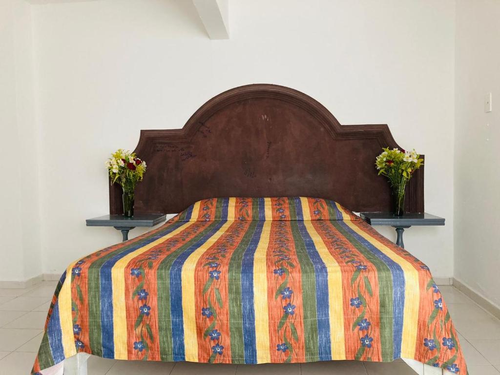 a bed with a colorful comforter and two tables with flowers at La Sirenita in Veracruz