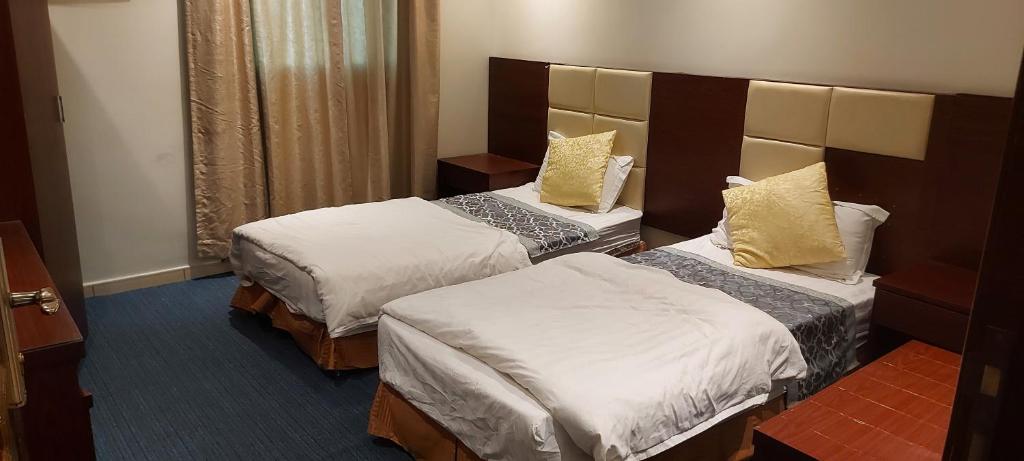 um quarto de hotel com duas camas com almofadas brancas e amarelas em نجمة العنان للشقق المخدومة em Tabuk