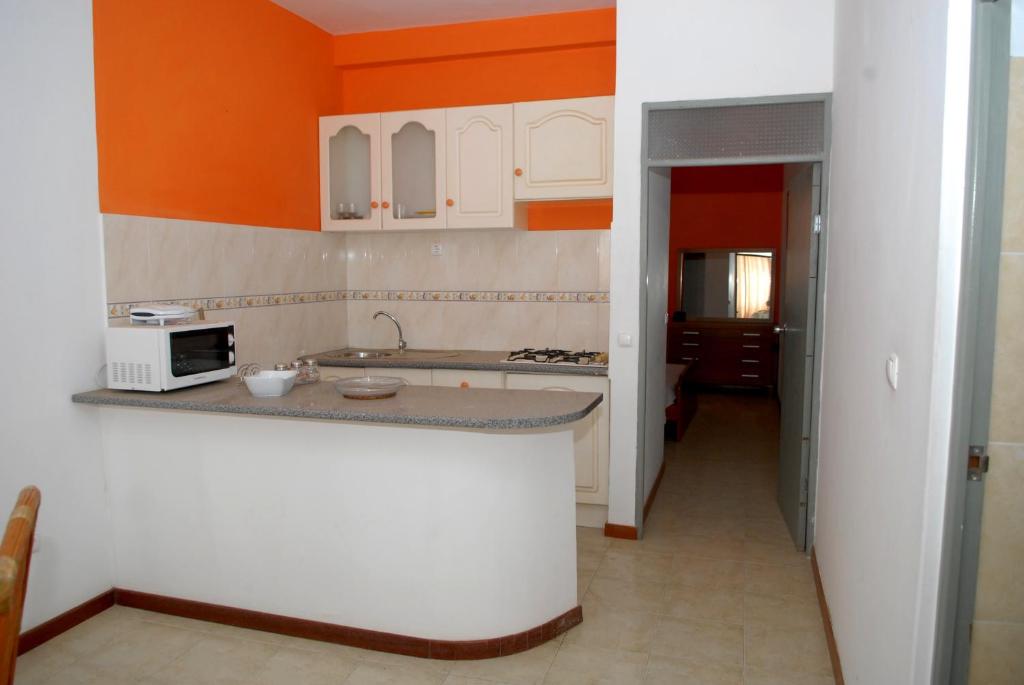 una cocina con armarios blancos y una pared de color naranja en Apartamentos Santiago - Praia en Praia