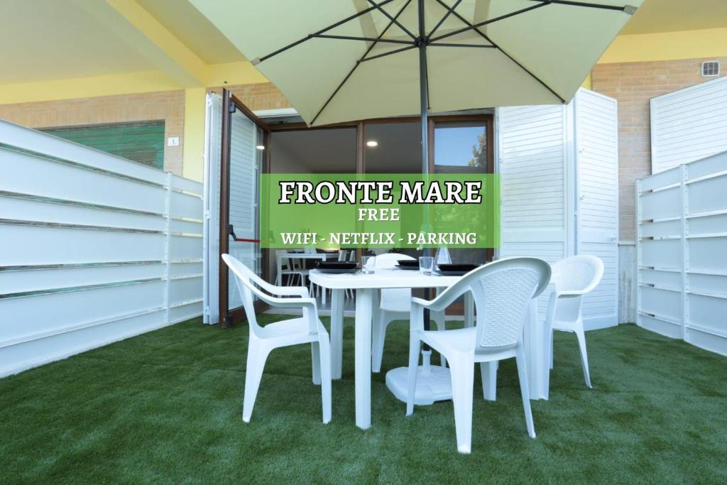 - une table avec des chaises blanches et un parasol sur la terrasse dans l'établissement NOVELLA DEL MAR prima fila dal mare, à Grottammare