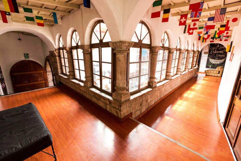 an empty room with windows and flags on the wall at Pirwa Backpackers Colonial in Cusco