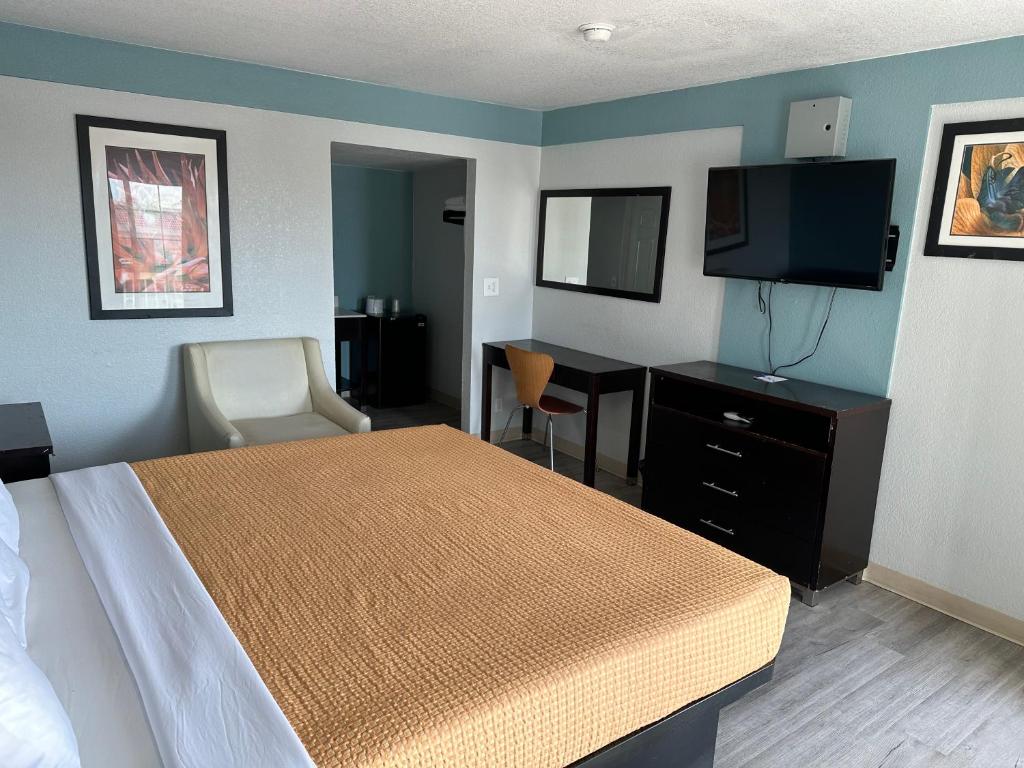 Habitación de hotel con cama, escritorio y TV. en Siesta Inn, en Fresno