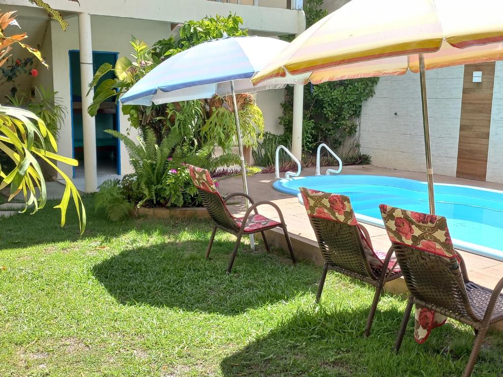 um grupo de cadeiras e guarda-sóis ao lado de uma piscina em Pousada Cajueiro em Itaúnas