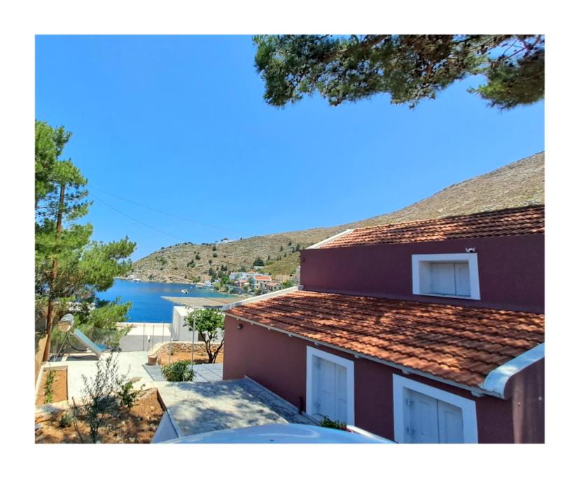 a red house with a roof with a view of the water at Villa Kochili. in Symi