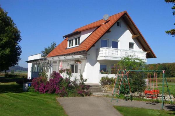 Biały dom z pomarańczowym dachem i huśtawką w obiekcie Ferienhaus Eichhölzle w mieście Münsingen