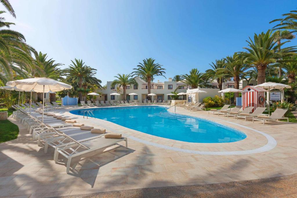 a swimming pool with lounge chairs and umbrellas at Alua Suites Fuerteventura - All Inclusive in Corralejo