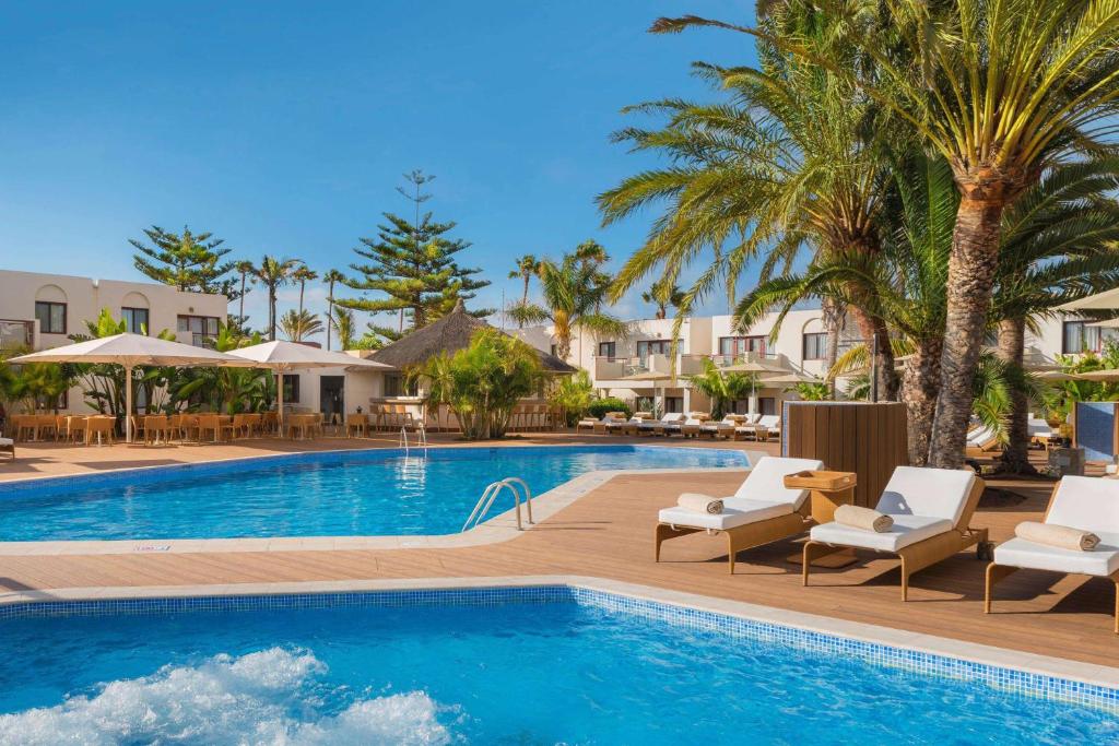 a pool at a resort with chairs and palm trees at Alua Suites Fuerteventura - All Inclusive in Corralejo