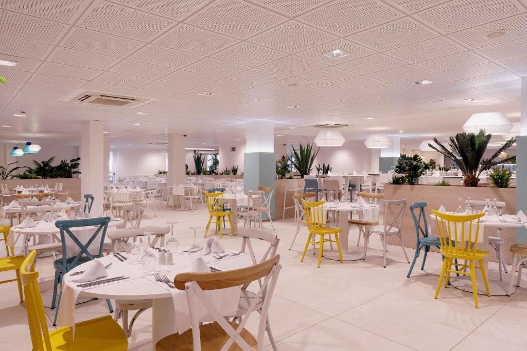 a dining room with white tables and yellow chairs at Alua Suites Fuerteventura - All Inclusive in Corralejo