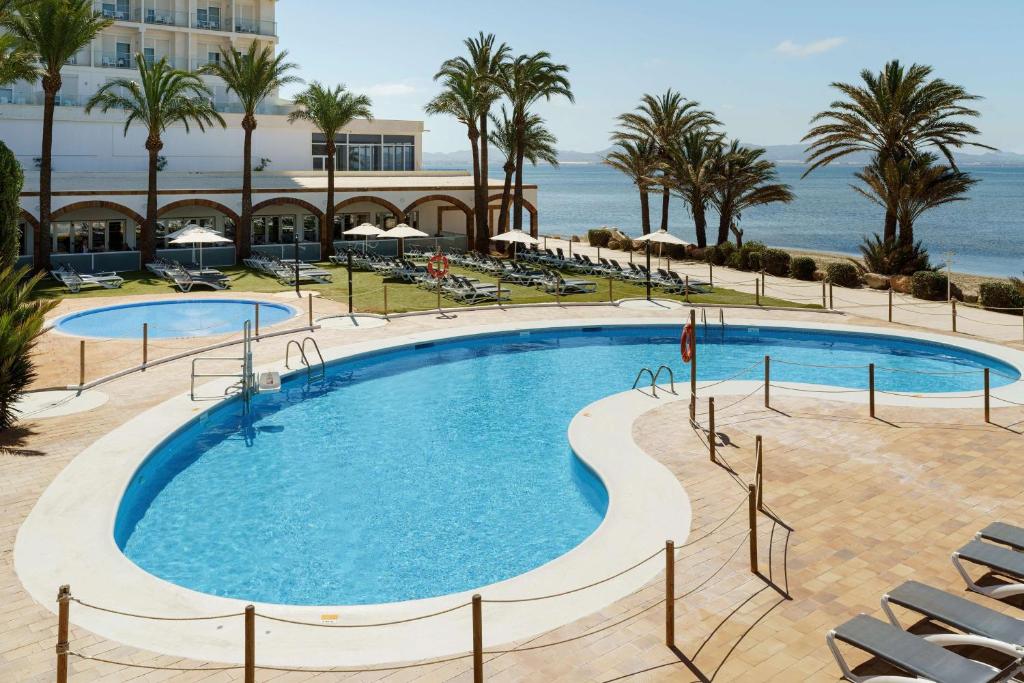 einen Pool mit Stühlen und das Meer im Hintergrund in der Unterkunft AluaSun Doblemar in La Manga del Mar Menor