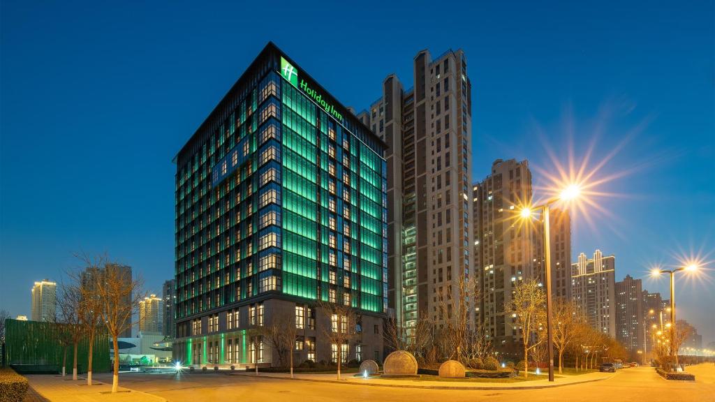 un grand bâtiment vert dans une ville la nuit dans l'établissement Holiday Inn Taiyuan Sunshine, an IHG Hotel, à Taiyuan