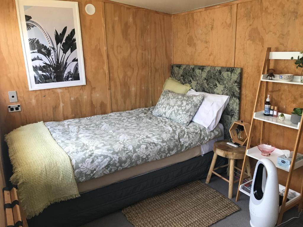 a small bedroom with a bed and a wooden wall at Minimalist Cabin Solo Traveller in Ashburton