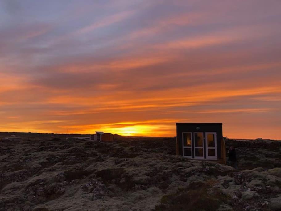 un pequeño edificio en un campo con la puesta de sol en el fondo en Lava mini houses, en Vogar